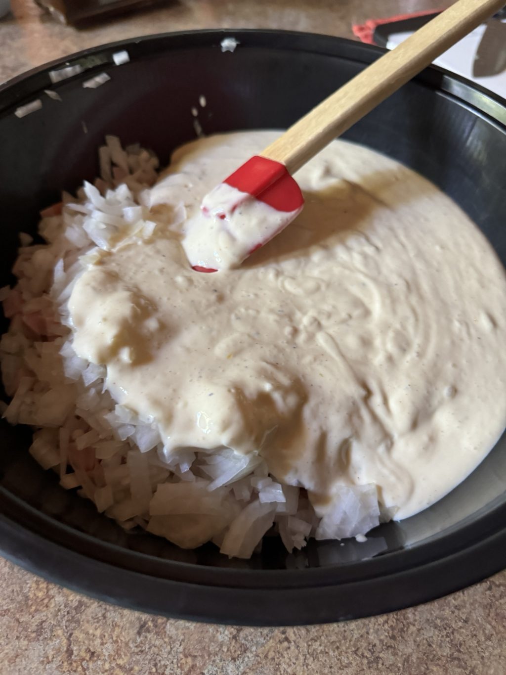 A pan of white sauce with chopped onions and a red spatula.