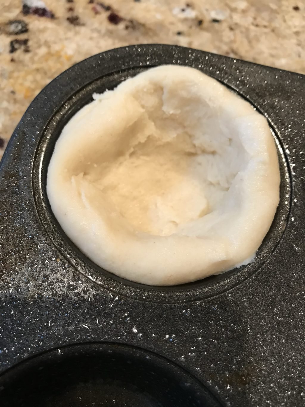Dough pressed into a muffin tin.