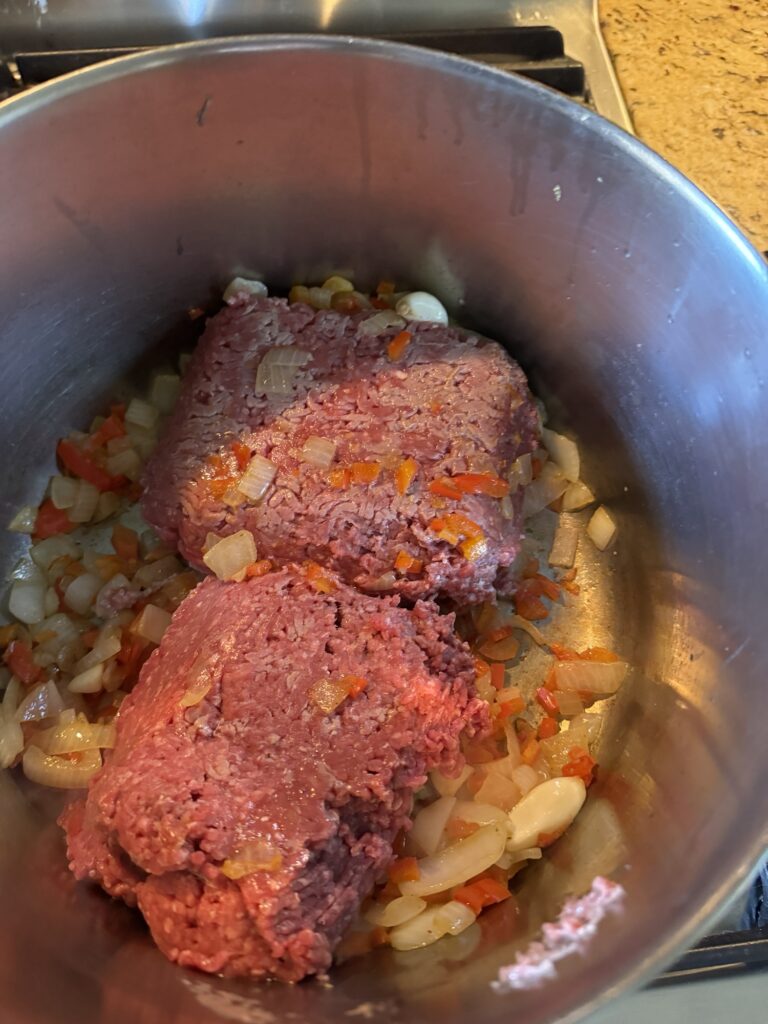 Two lumps of ground beef in a pot with tomatoes, onions, and garlic