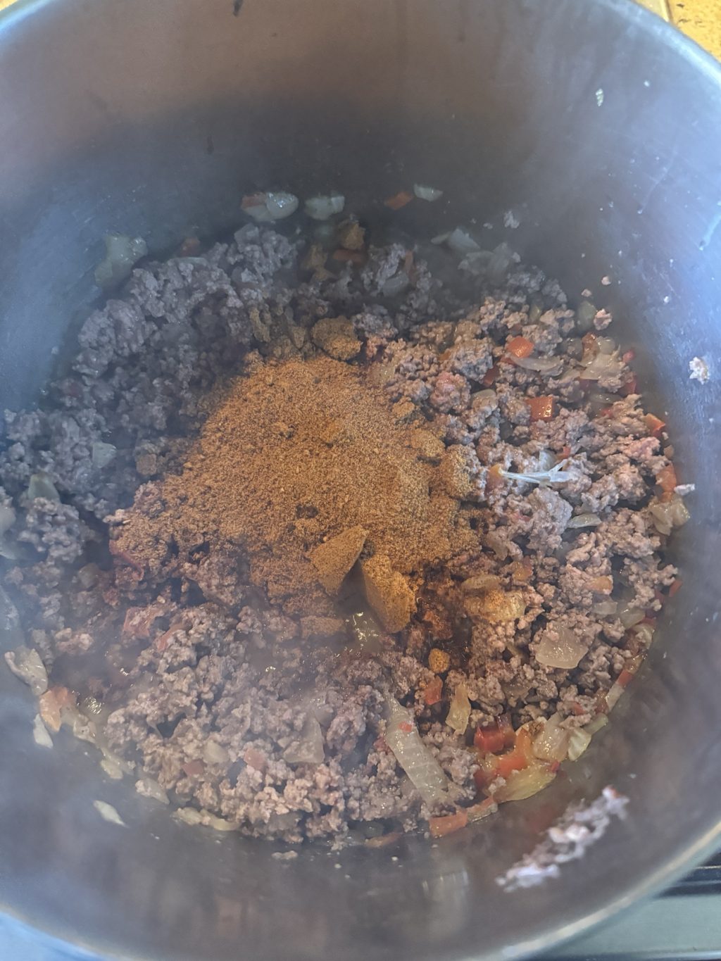 Seasonings over ground meat, tomatoes, and onion in a pot