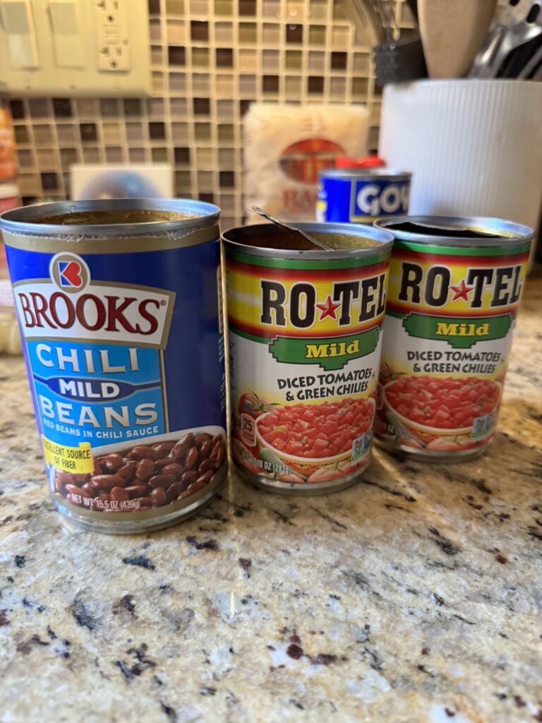 One can of chili beans next to two cans of diced tomatoes and green chilis