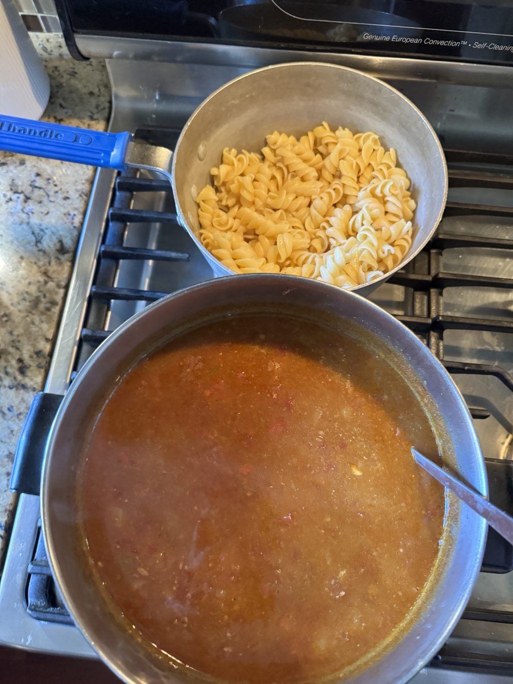 The pot of soup next to a pot of rotini noodles