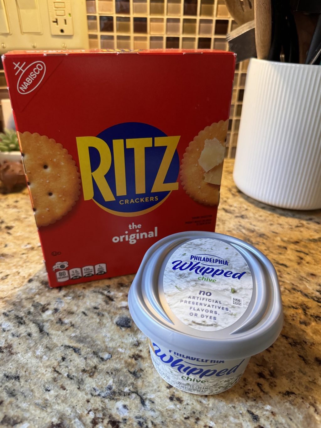 A box of Ritz crackers next to a container of whipped Philadelphia cream cheese with chive.