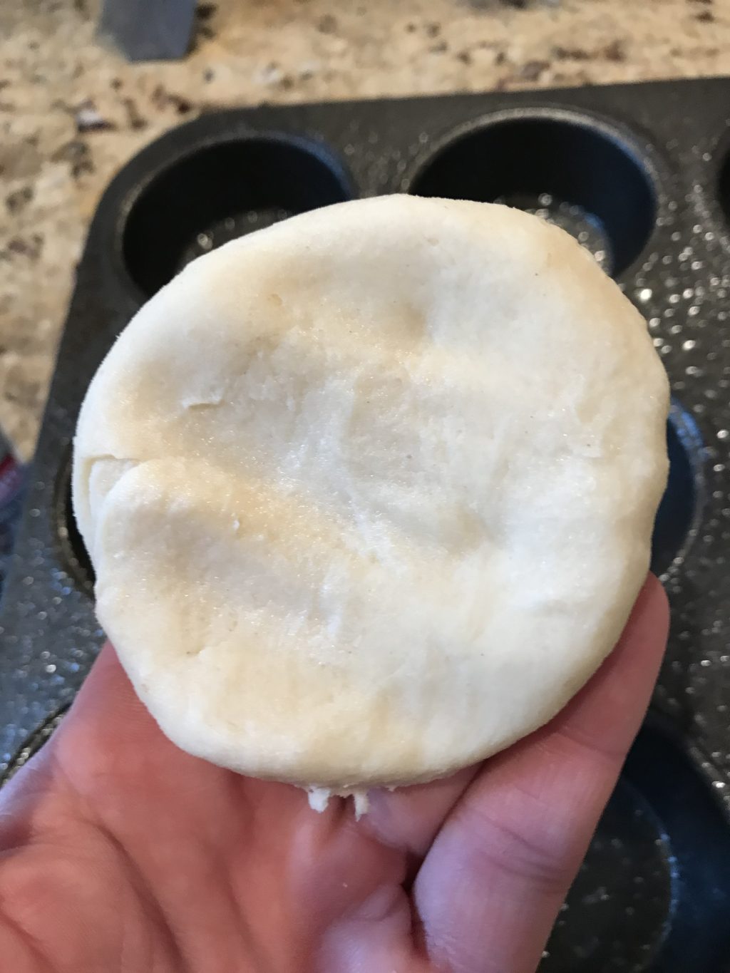 A circe of dough held above a muffin tray.