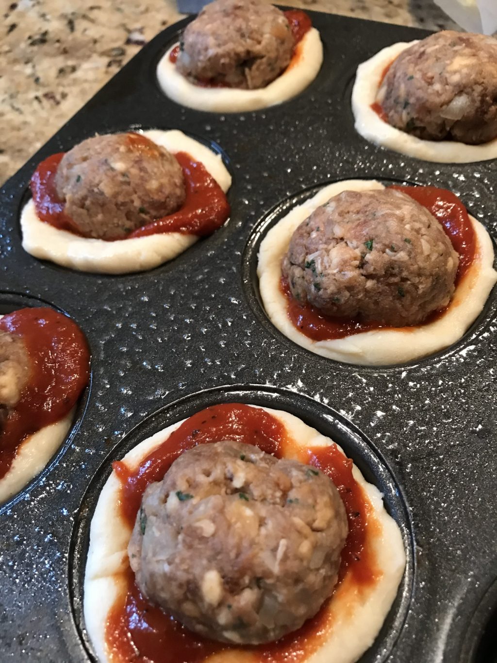 Raw meatballs in sauce in the raw dough in the muffin tin.
