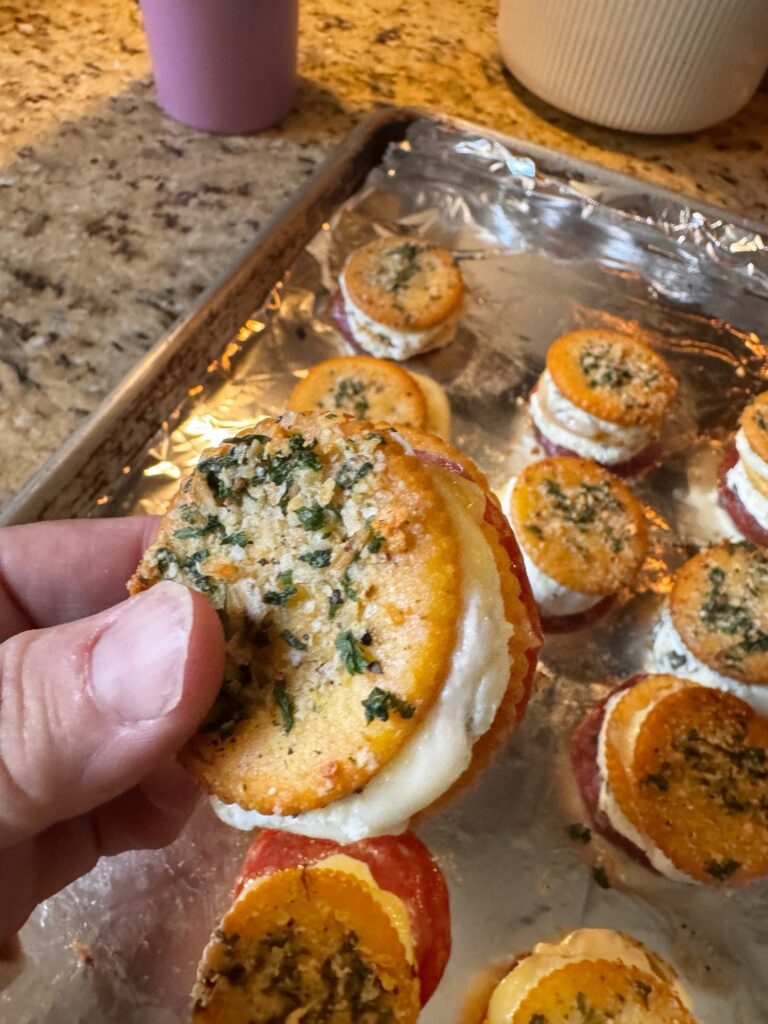 A close up of a finished Baked Cheesy Cracker Snack held above a tray of others.