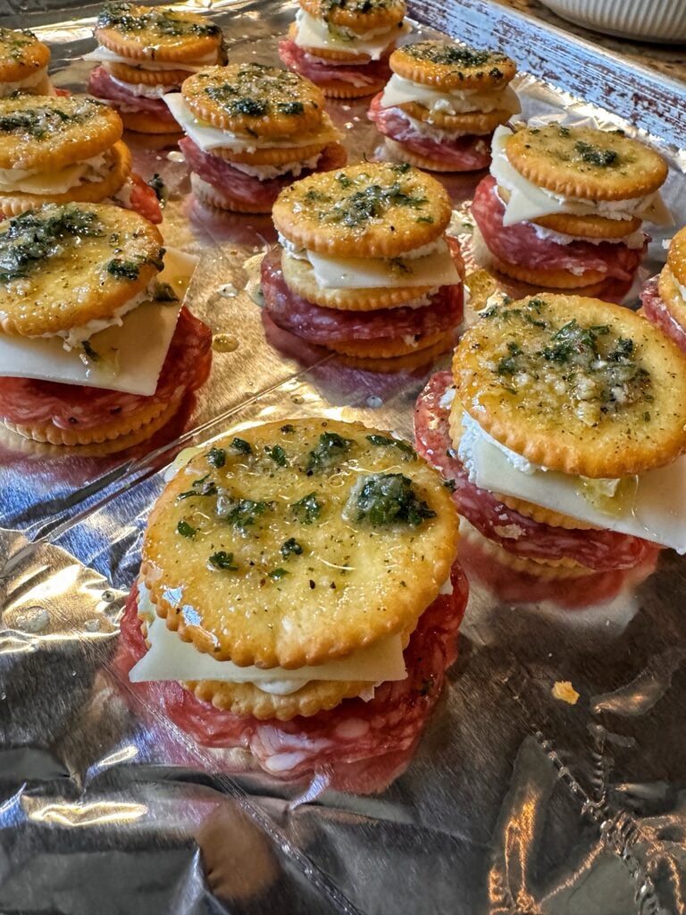 A tray of baked cheesy cracker snacks. They are baked double decker cracker sandwiches with salami and cheese inside.