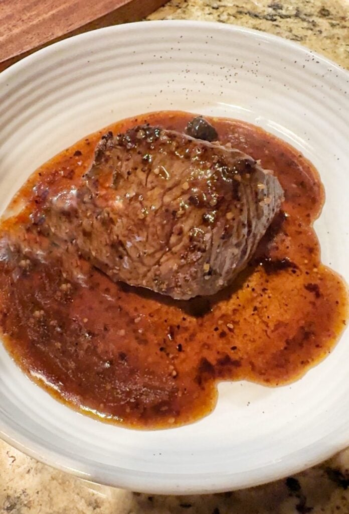 A sirloin steak in a pool of gravy on a plate.