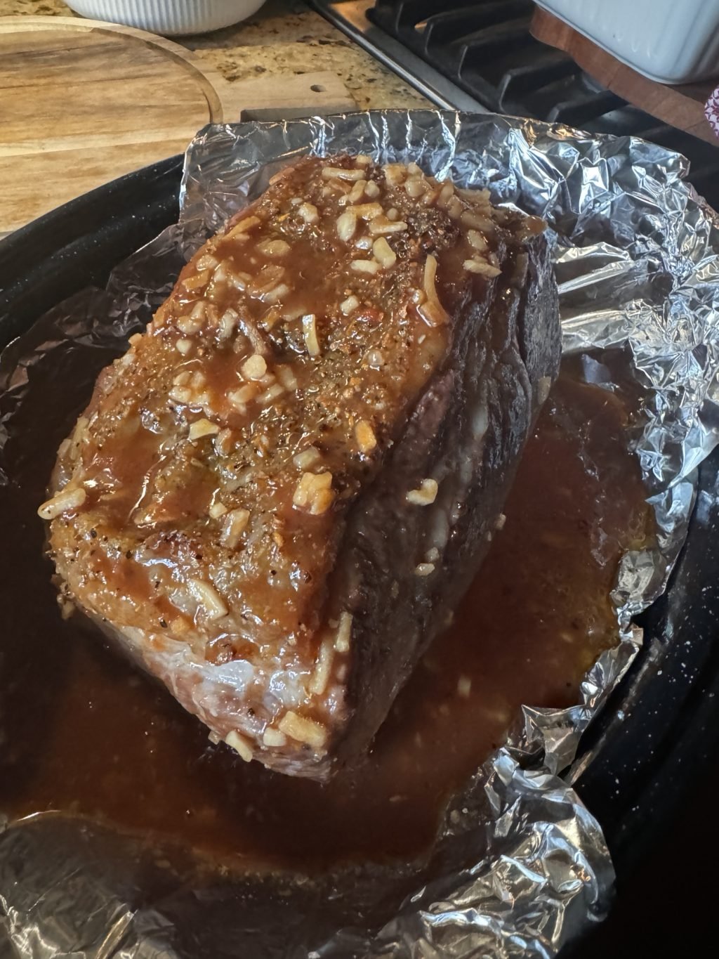 The beef roast covered in sauce in an aluminum foil covered baking dish.