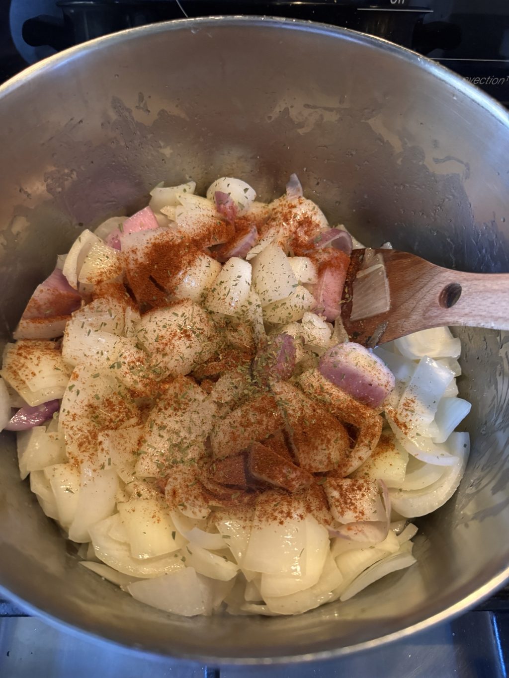Sliced onions covered in spices in a pot with a wooden spoon.