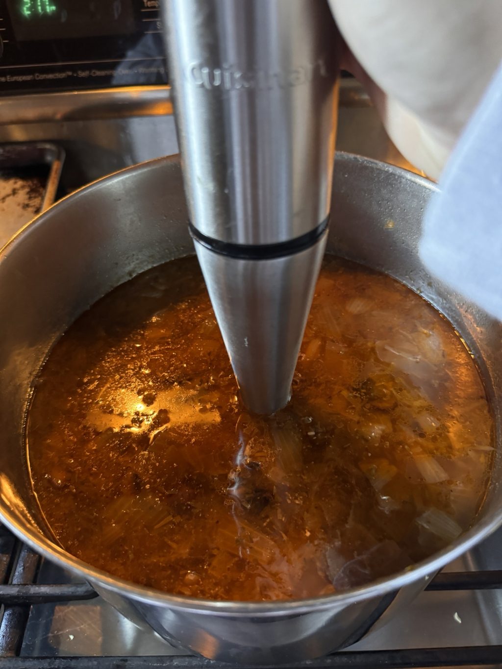 An immersion blender in the soup mixture in a pot.