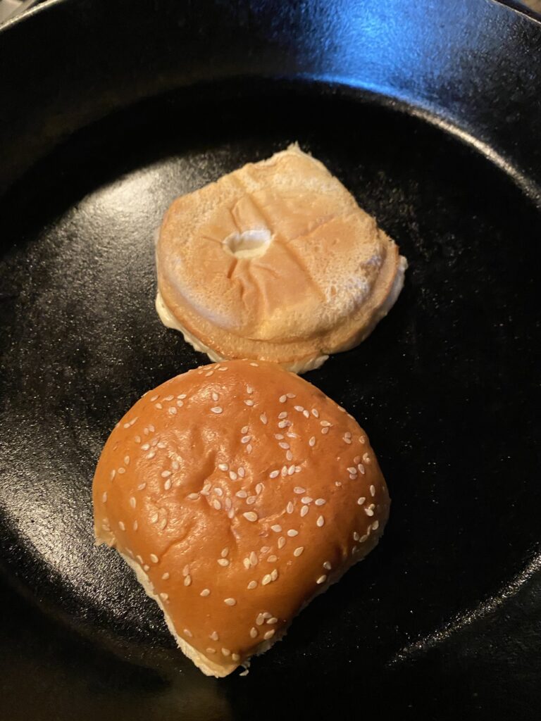 A sesame bun being toasted on a cast iron skillet.