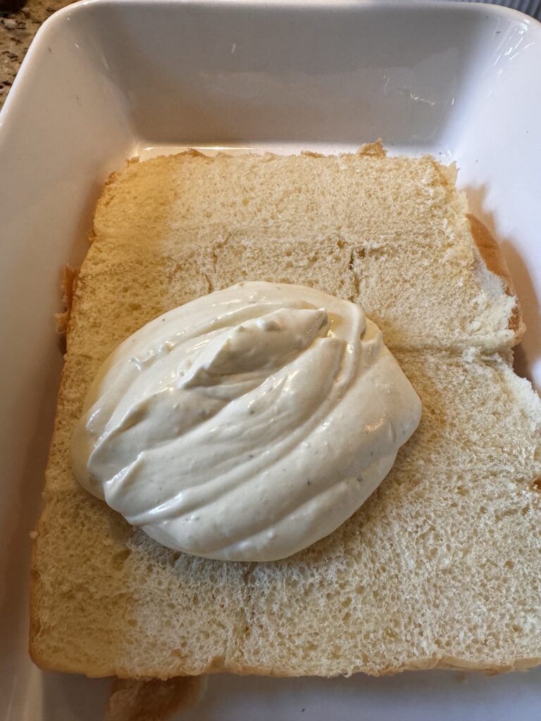 A slab of King's Hawaiian Rolls with the top half removed with a large dollop of garlic cream cheese mixture on top.