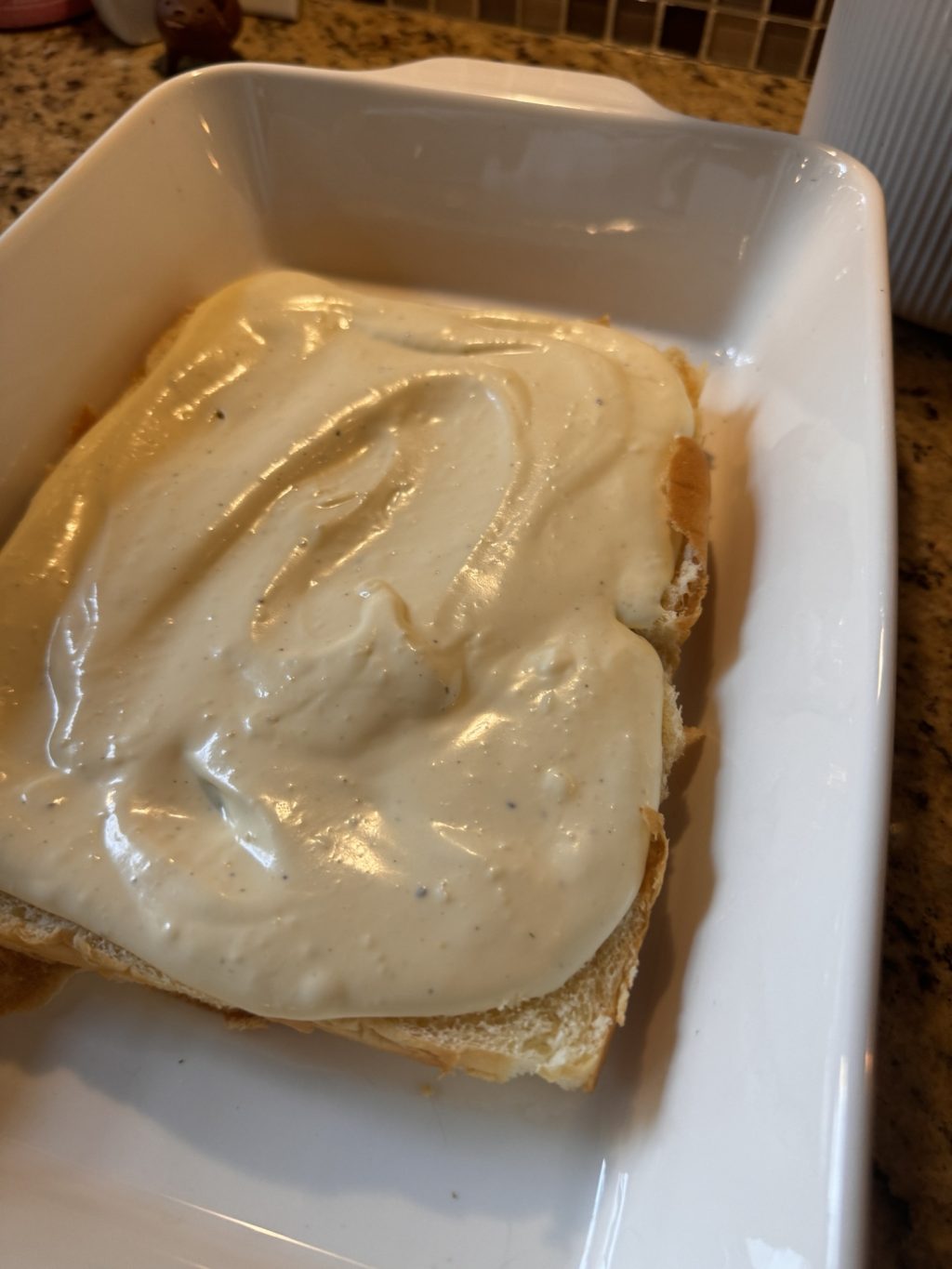 The half slab of Hawaiian Rolls with the cream cheese mixture spread out over it in a baking dish.