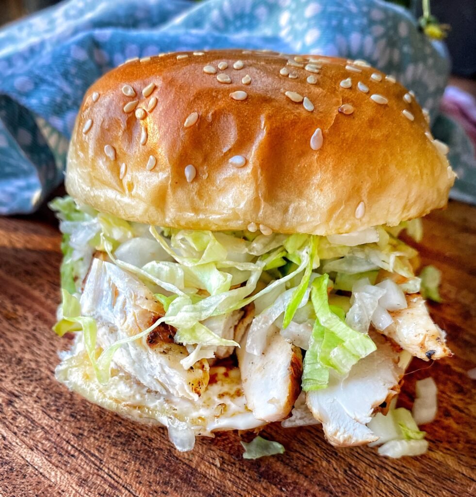 A grilled chicken sandwich with shredded lettuce on a sesame seed bun.
