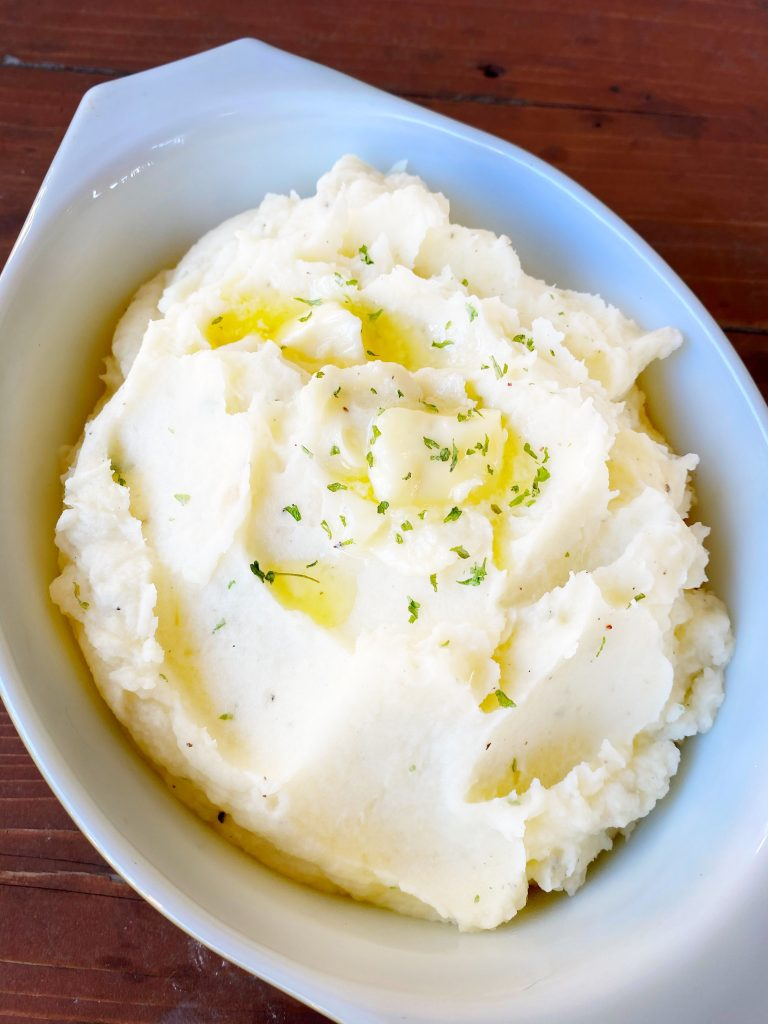 Mashed potatoes in a white dish with green garnish.