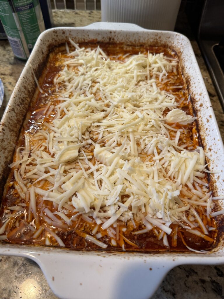A baking dish filled with marinara sauce and covered in shredded cheese.