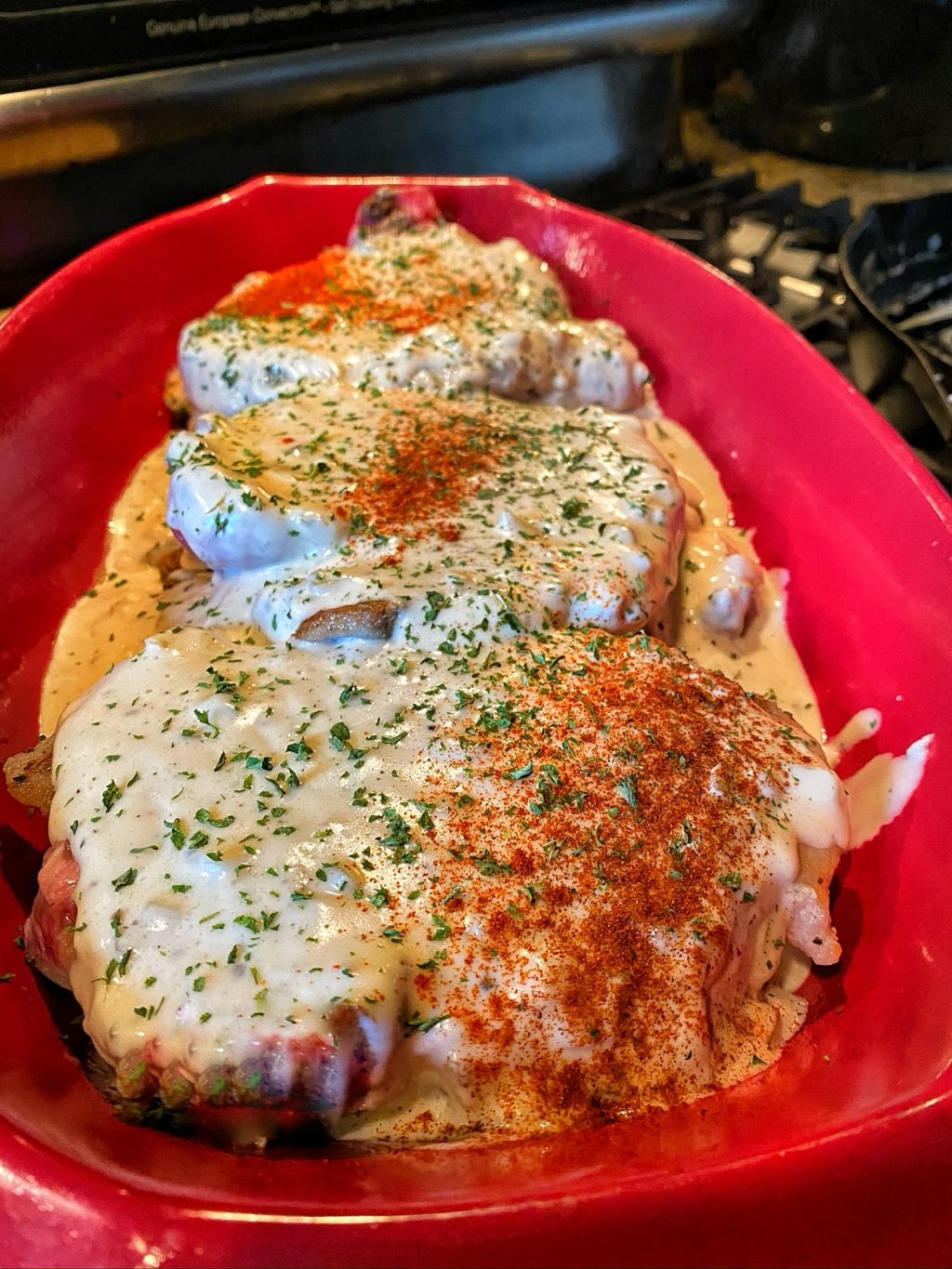 Raw pork chops in a red baking dish topped with white gravy and stuffing.
