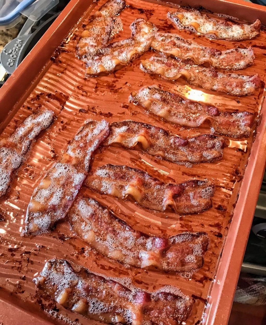 Cooked bacon on a bacon pan filed with delicious bacon grease.
