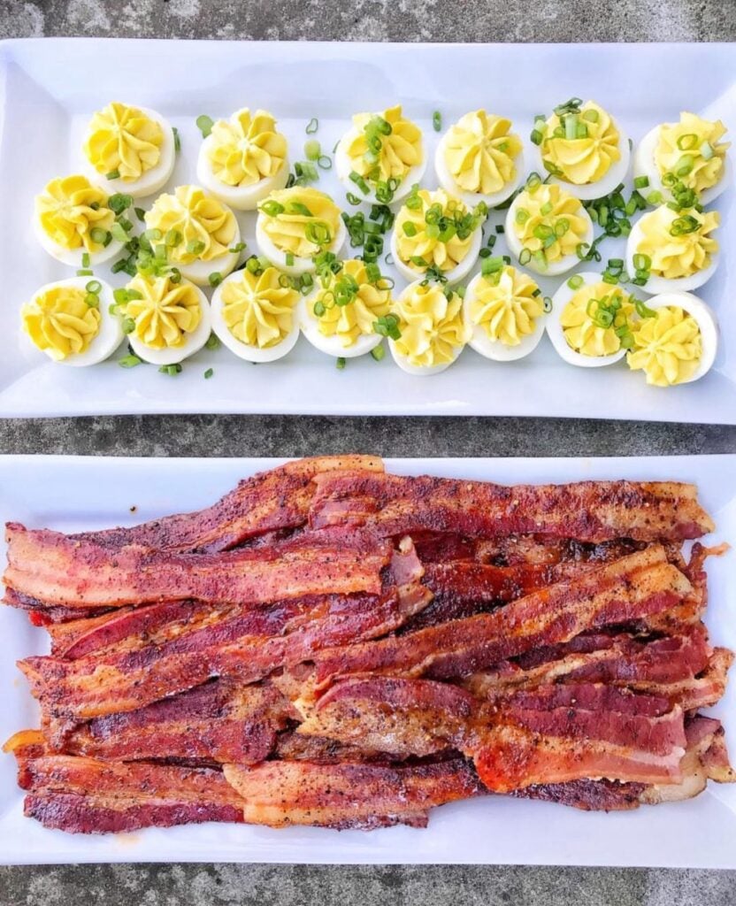 A rectangular plate of deviled eggs on a counter above a rectangular plate of candied bacon.