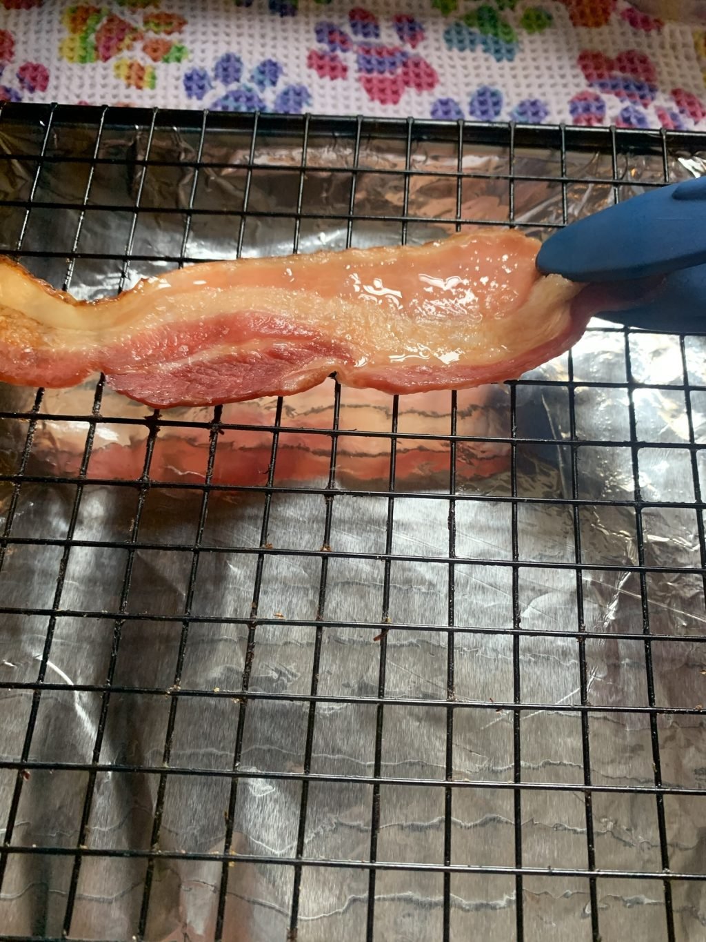 A slice of precooked floppy bacon being placed on the baking grate with tongs.