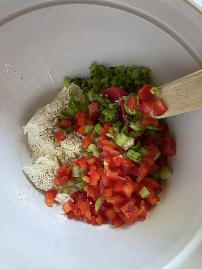 The dip ingredients, including diced red peppers and green onion, in a bowl with a spatula.