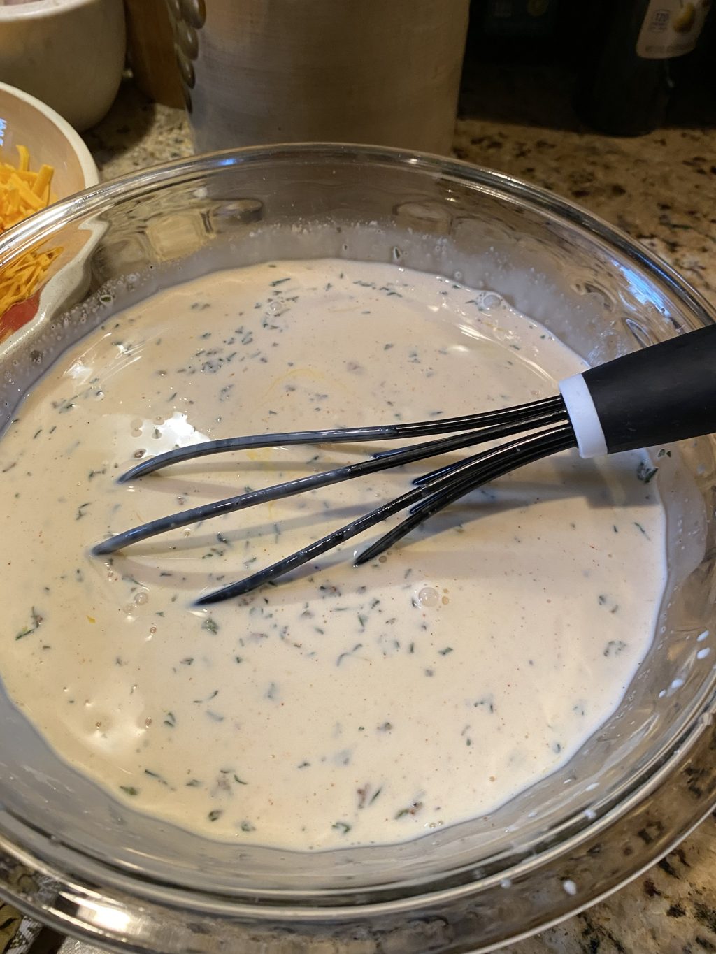 A white gravy mixture in a glass with a whisk placed in it.