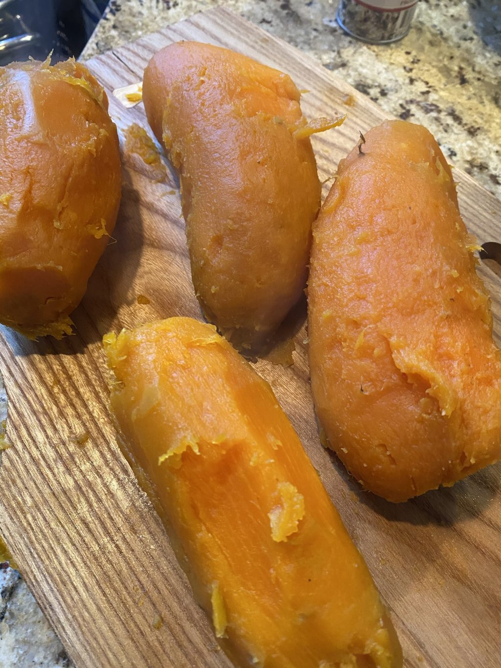 Peeled, cooked sweet potatoes on a wooden cutting board.