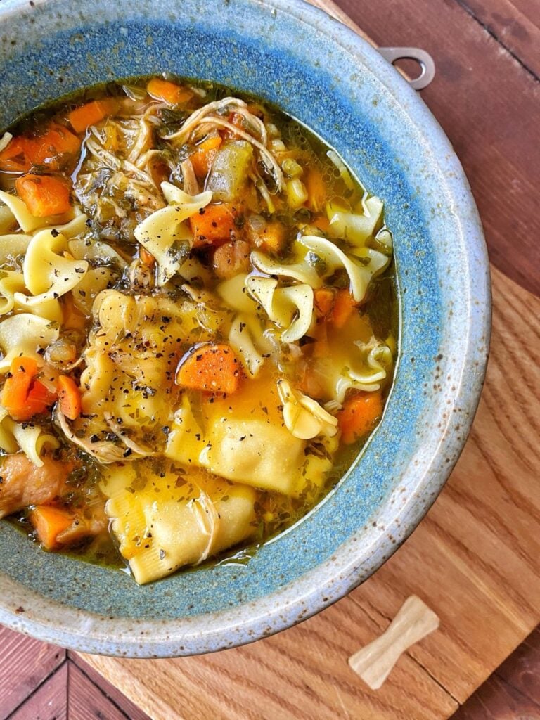 Chicken noodle soup in a blue, ceramic bowl.