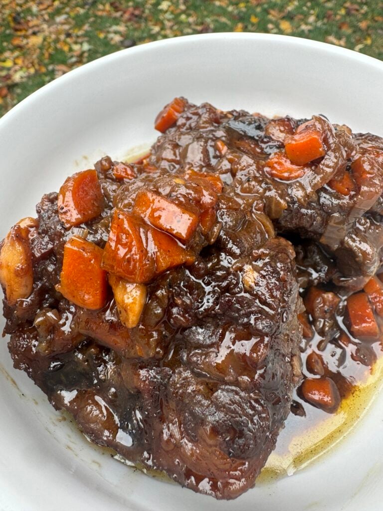 Braised oxtails on a white plate with savory gravy and carrots.