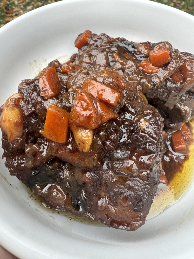 Braised oxtails on a white plate with savory gravy and carrots.