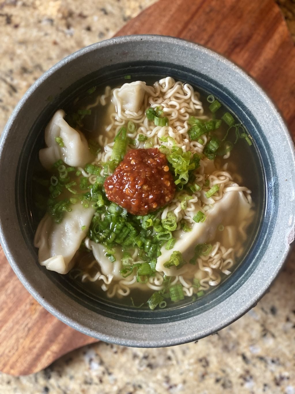 An overhead view of the noodle and dumpling soup with green onion and chili sauce on top.