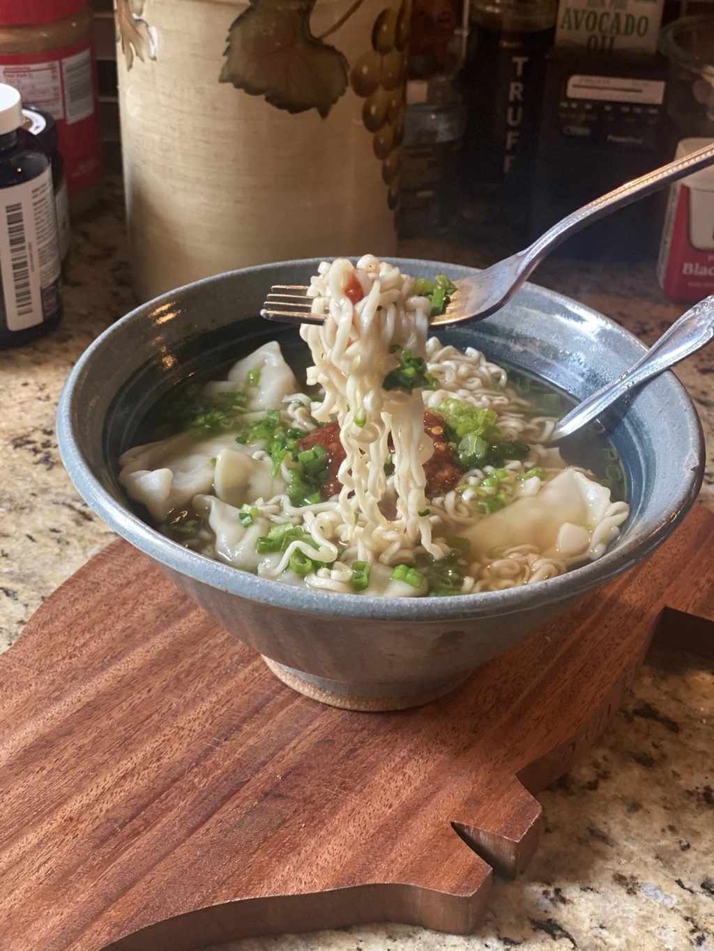 A forkful of noodles being lifted above a bowl of noodle and dumpling soup.