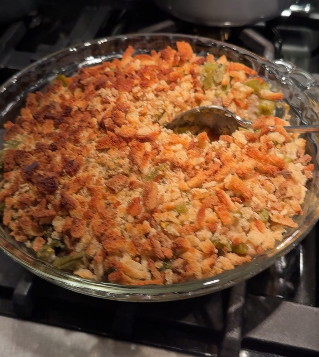 Green bean casserole in a glass dish with a spoon scooping into it.