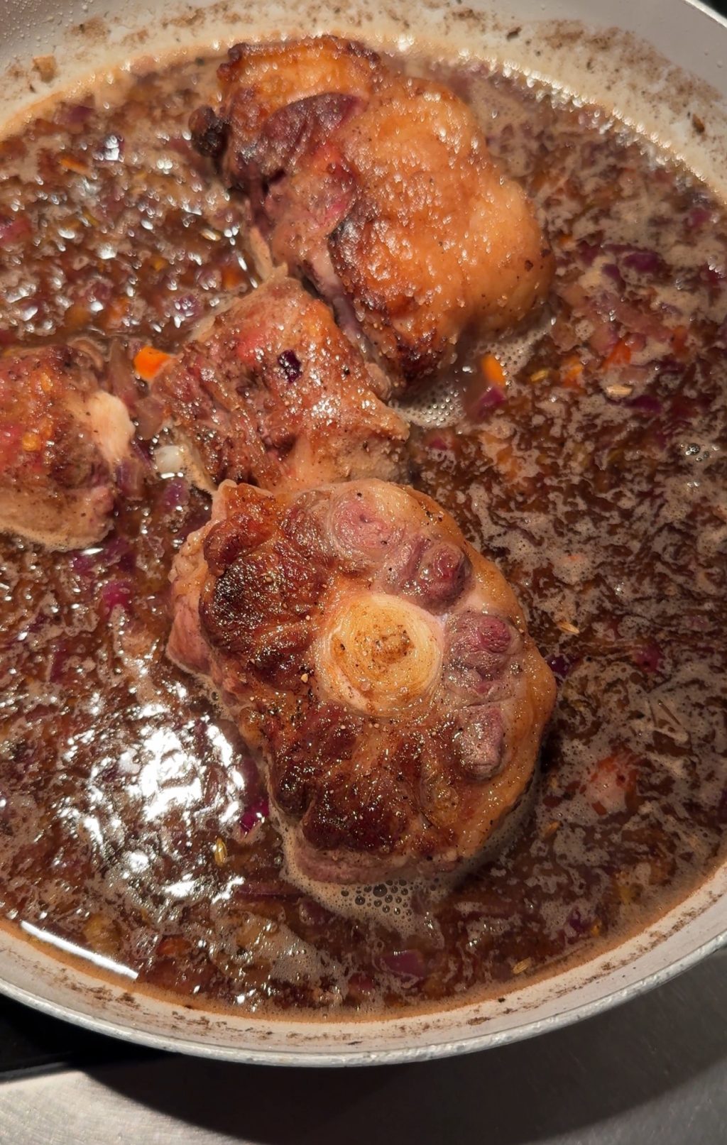 Ox tails cooking in gravy in a pan.