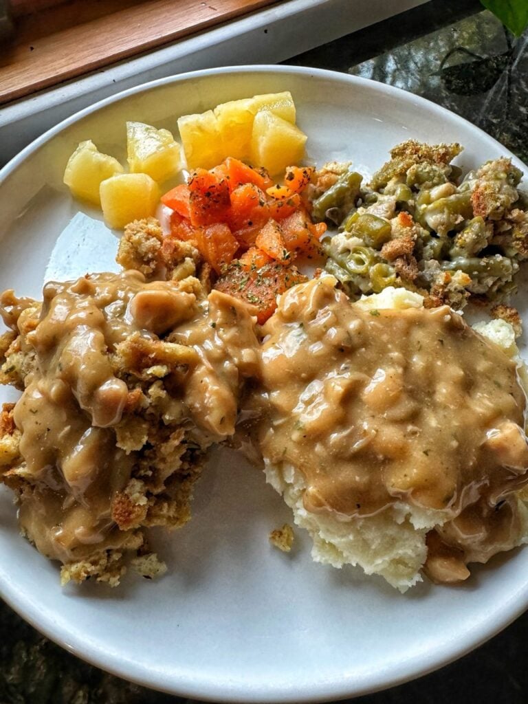 Stuffing, mashed potatoes, and Thanksgiving veggies covered in gravy on a white plate.