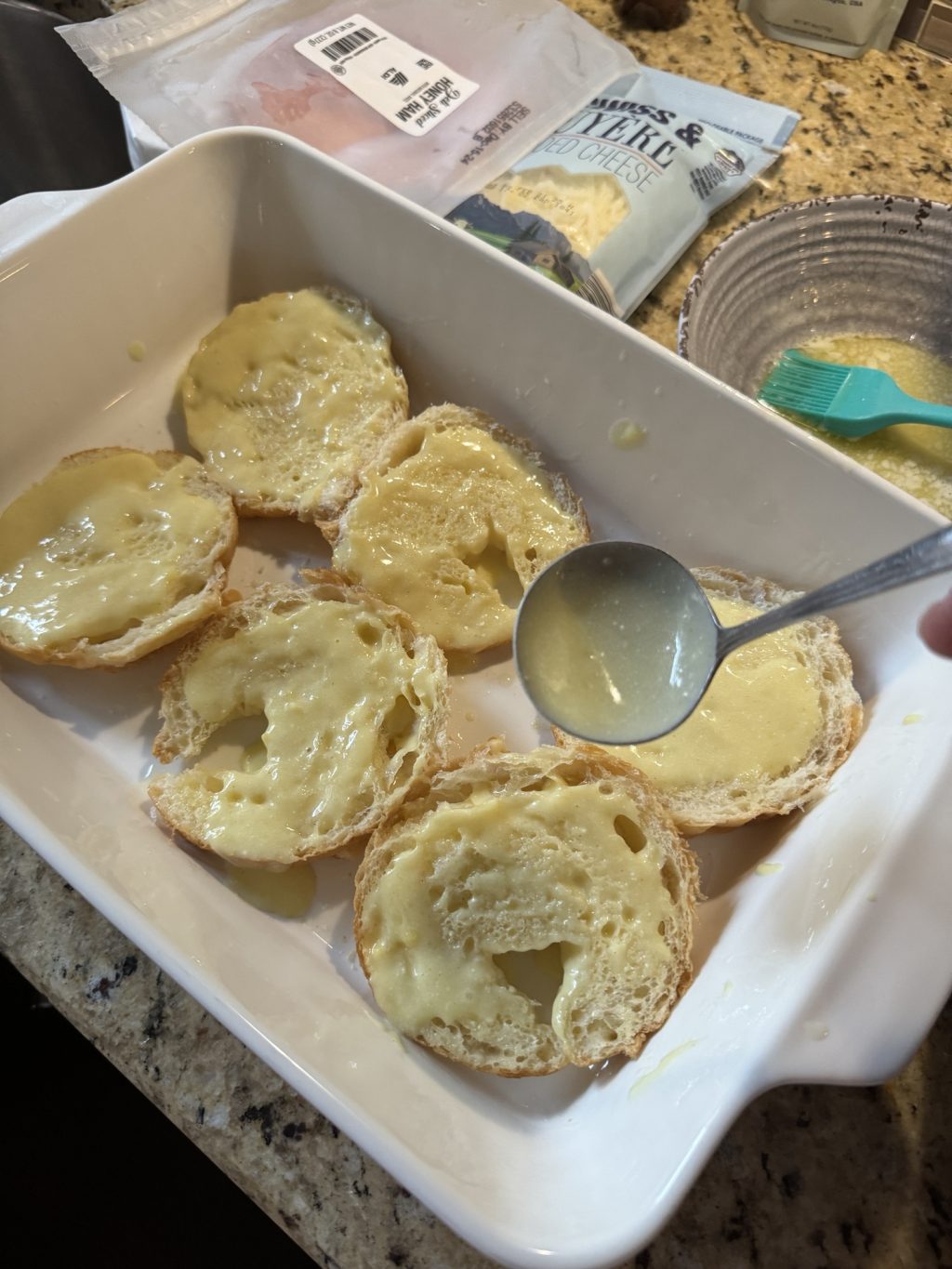 Sliced croissant halves in a baking dish being drizzled with melted butter and hollandaise. 