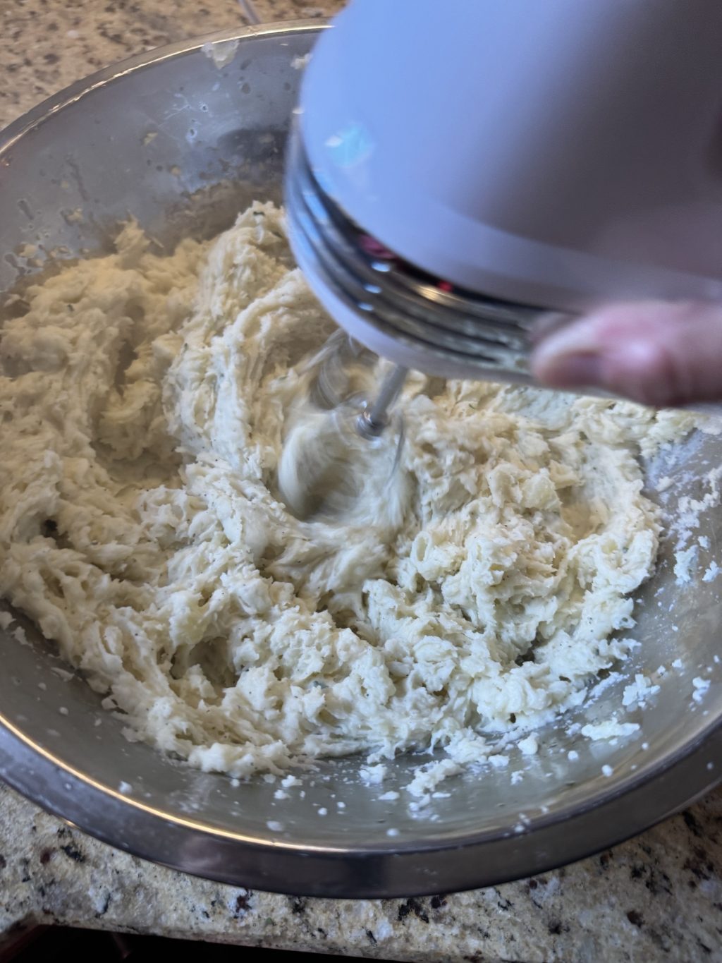 Potatoes in a metal bowl being mashed with a hand mixer.