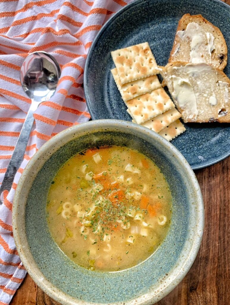 A bowl of After School soup next to a plate of crackers and buttered bread