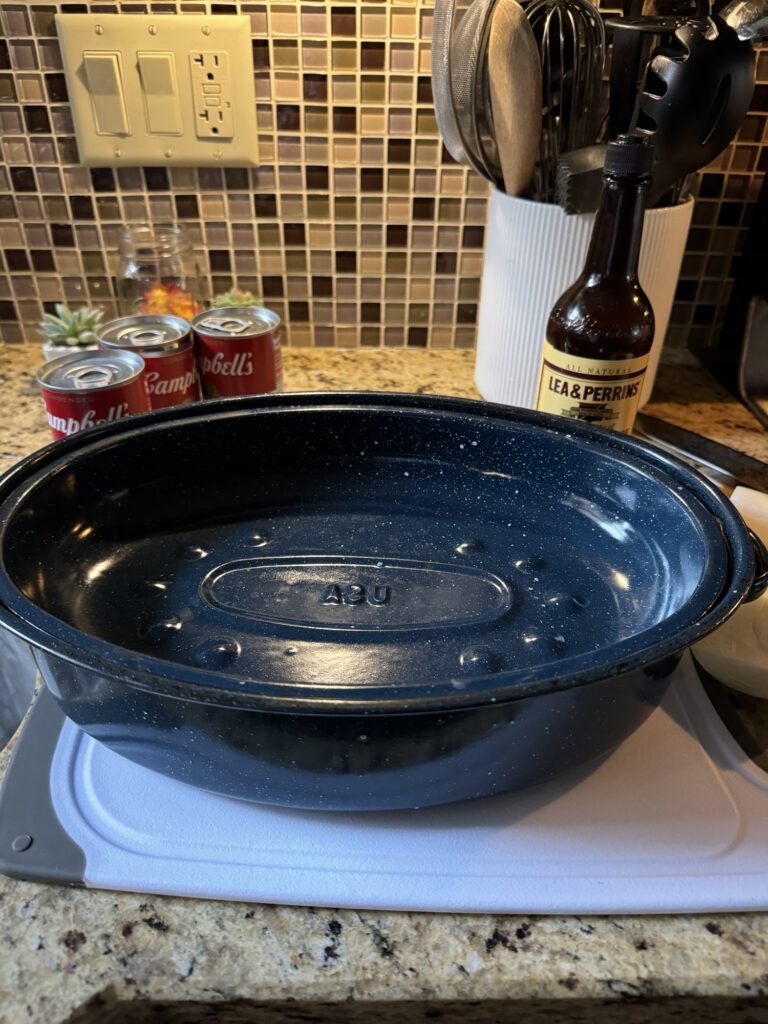 An empty blue specked roaster on a counter next to cans of Campbell's Soup and Worcestershire Sauce.