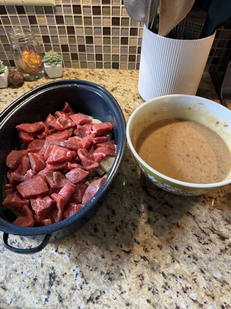 Raw pieces of cut steak in the blue speckled roaster next to a bowl of gravy.