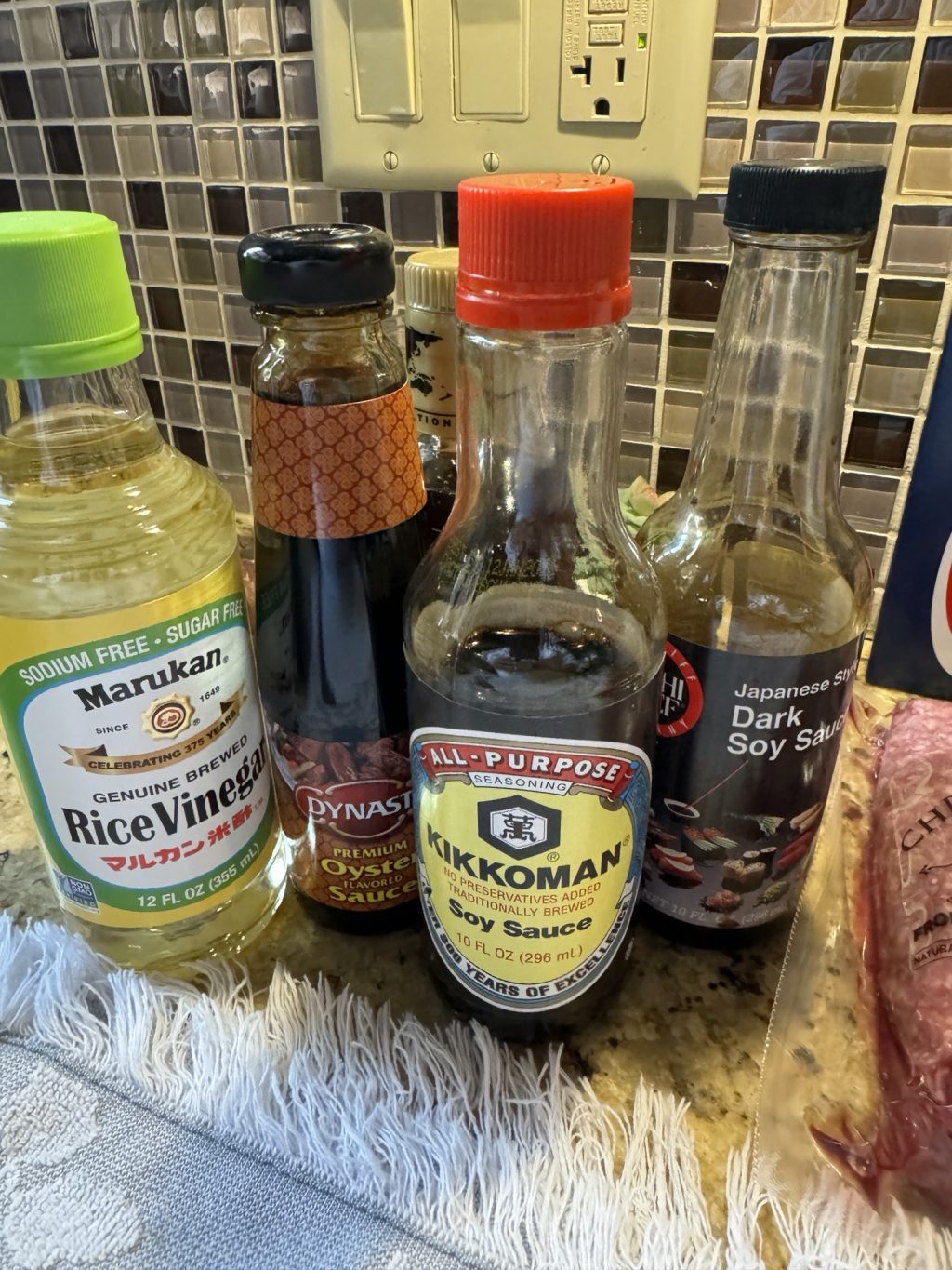 Bottles of rice vinegar, oyster sauce, soy sauce, and dark soy sauce on a counter.