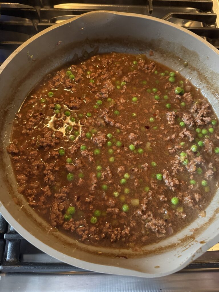 A pan with ground meat, peas, and sauce.