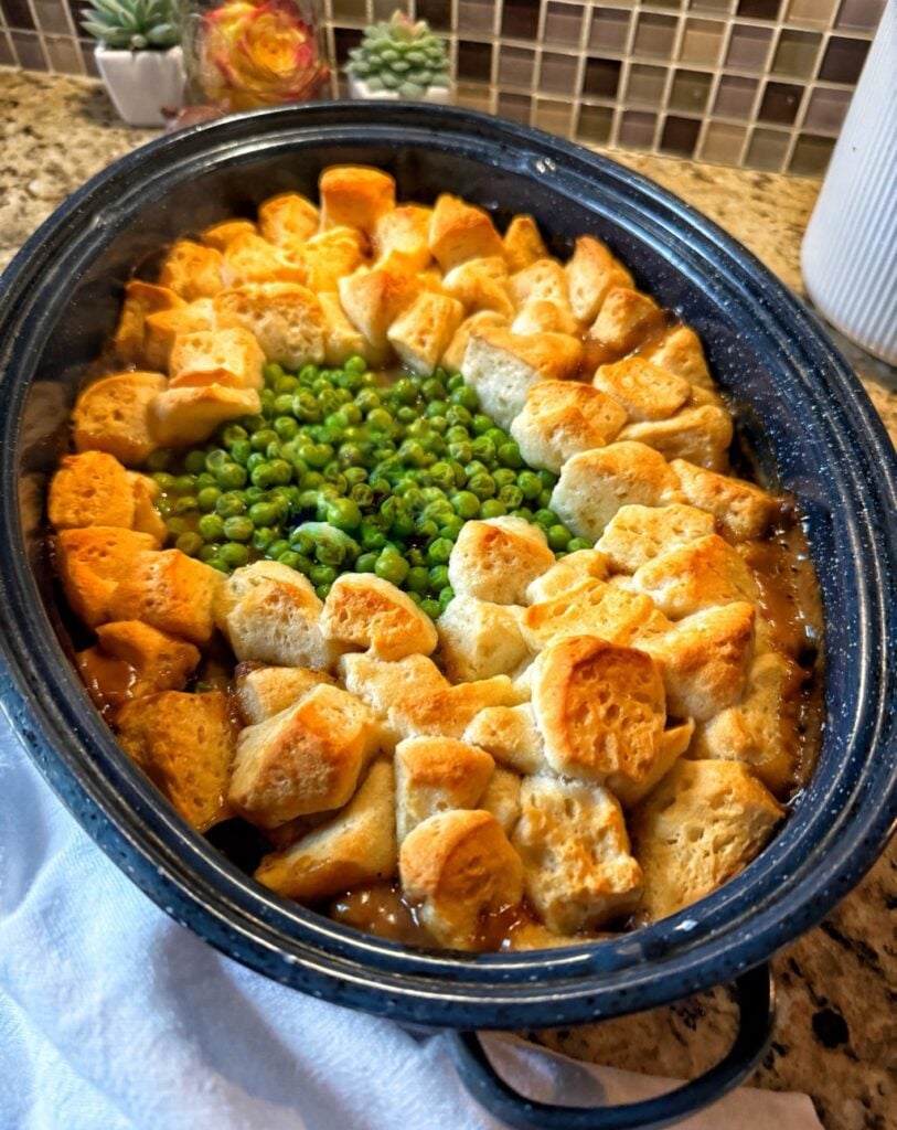 Bread dumplings in a blue slow cooker surrounding peas over beef.