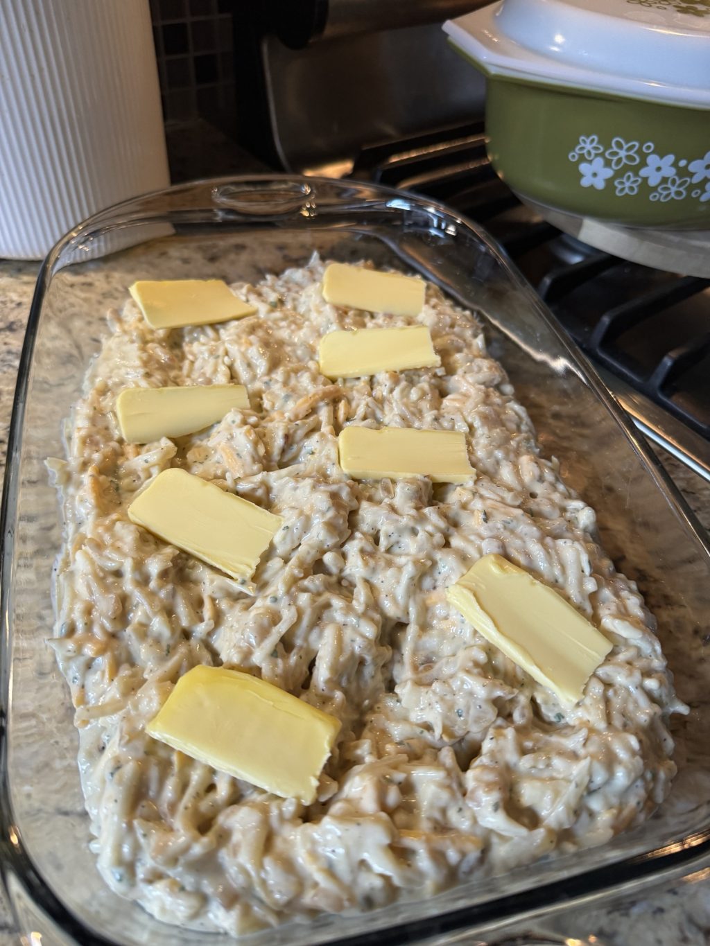 Pats of butter on the hash brown casserole in a glass dish before it bakes