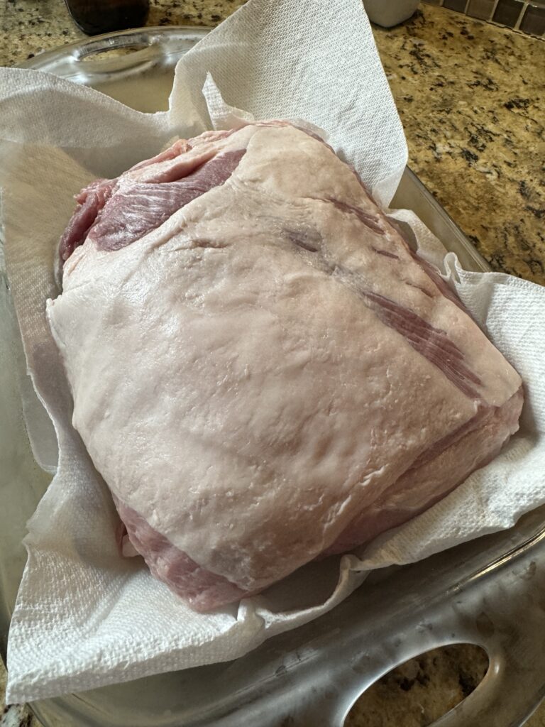 The frenched pork roast removed from the packaging and placed on a paper towel in a glass baking dish.