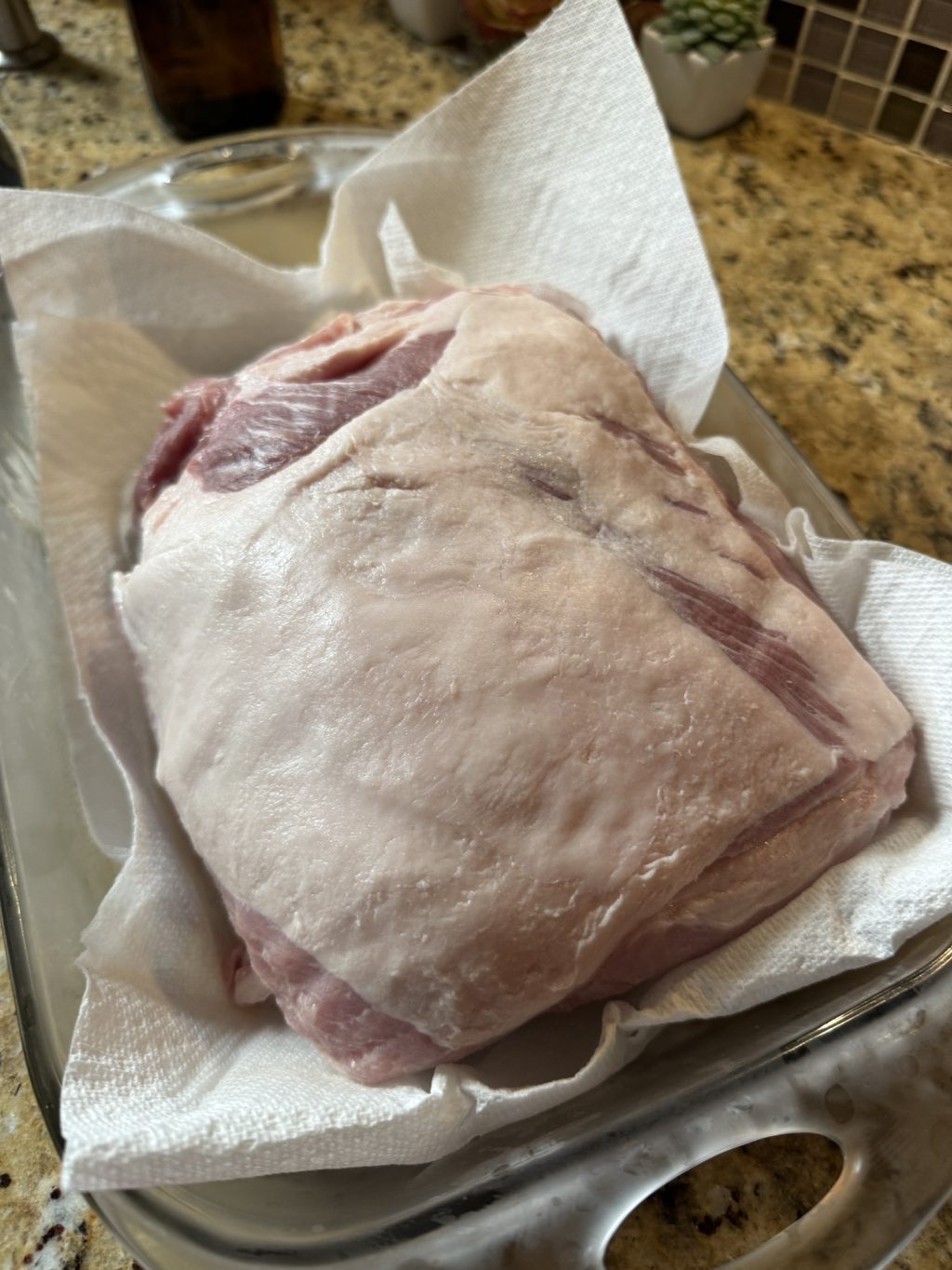 The pork roast on paper towel in a glass baking dish