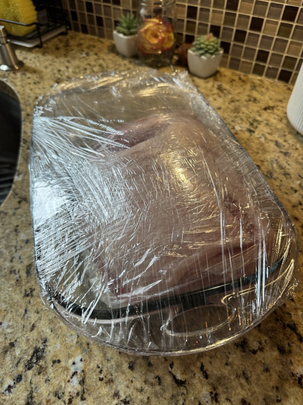 Pork roast in a glass baking baking dish wrapped in plastic wrap