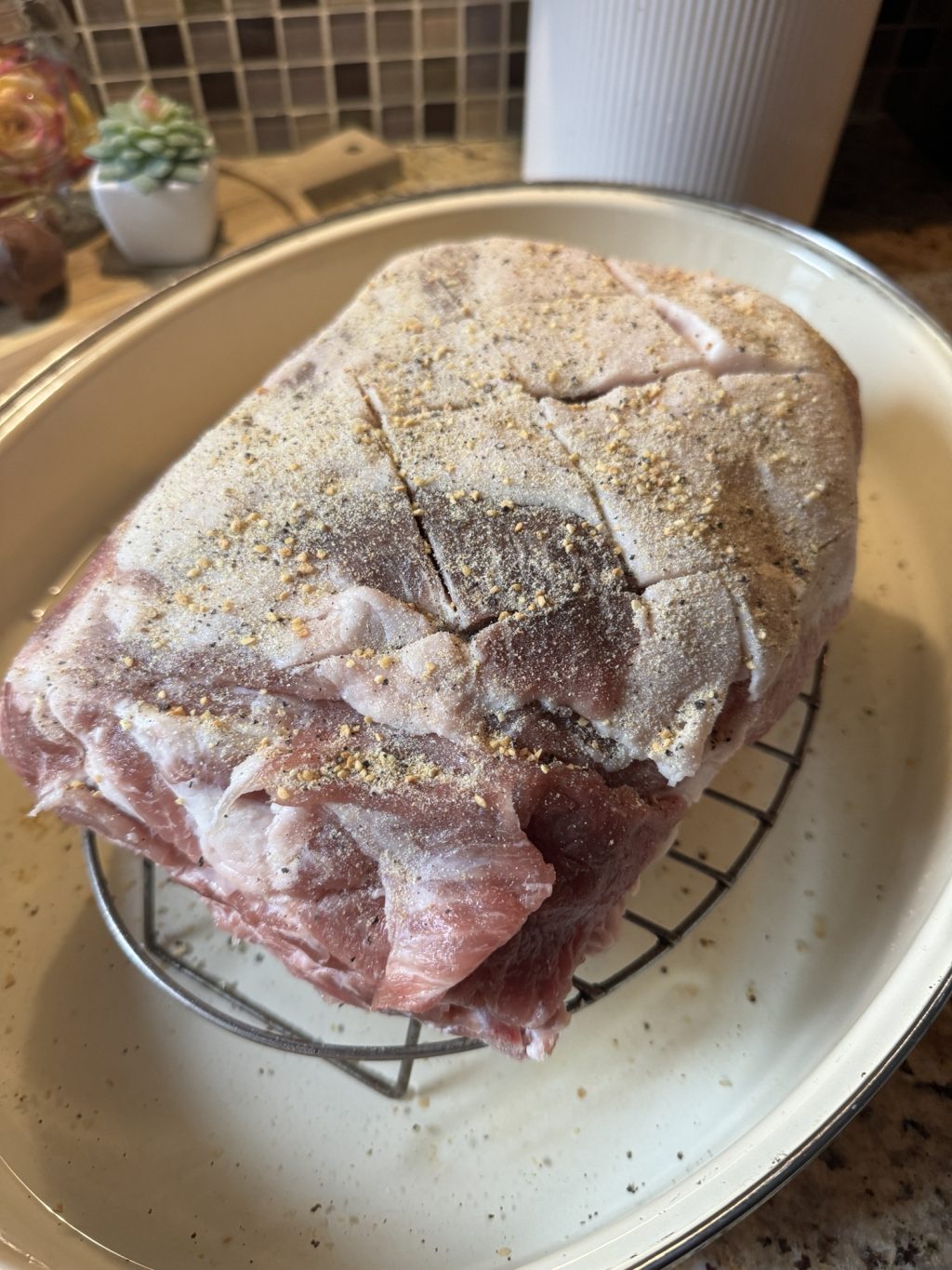Scored and seasoned pork roast on a baking rack in a baking dish before being put into the oven