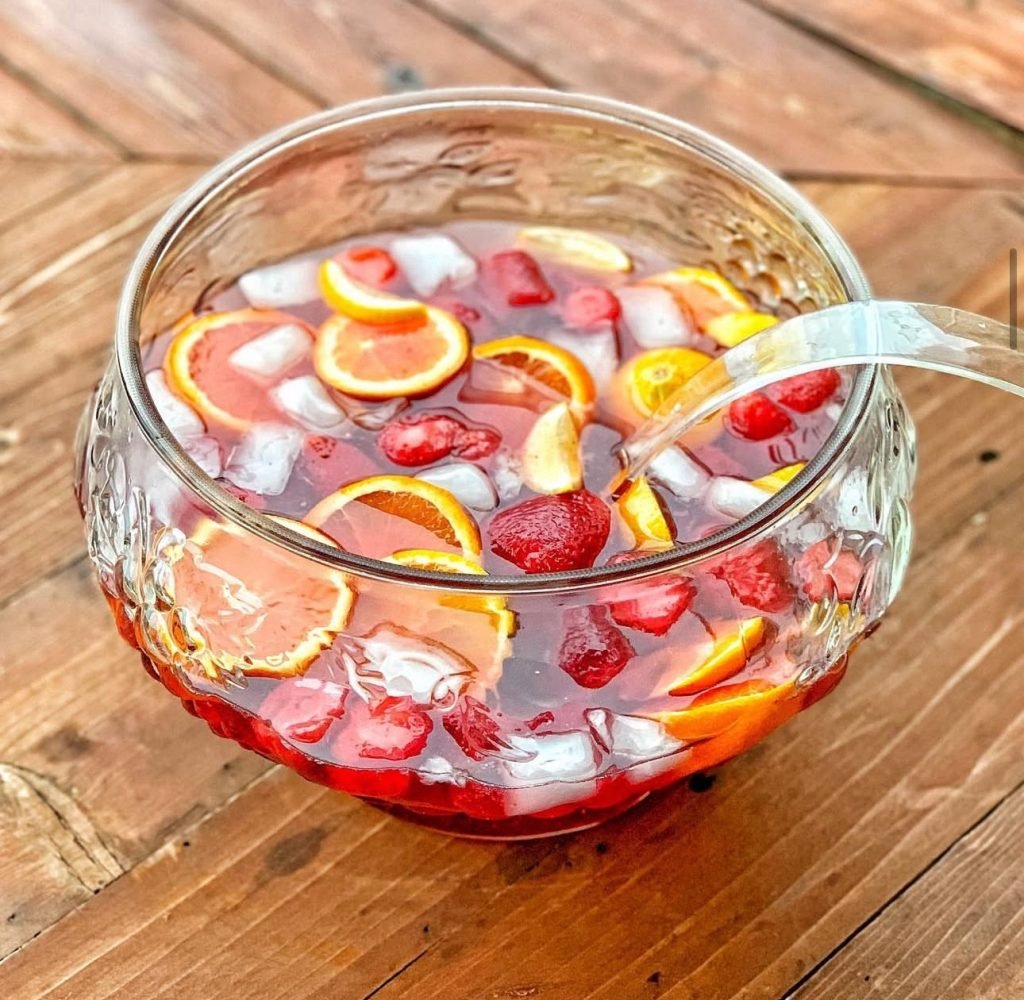 A glass bowl of party punch with fruit and ice in it